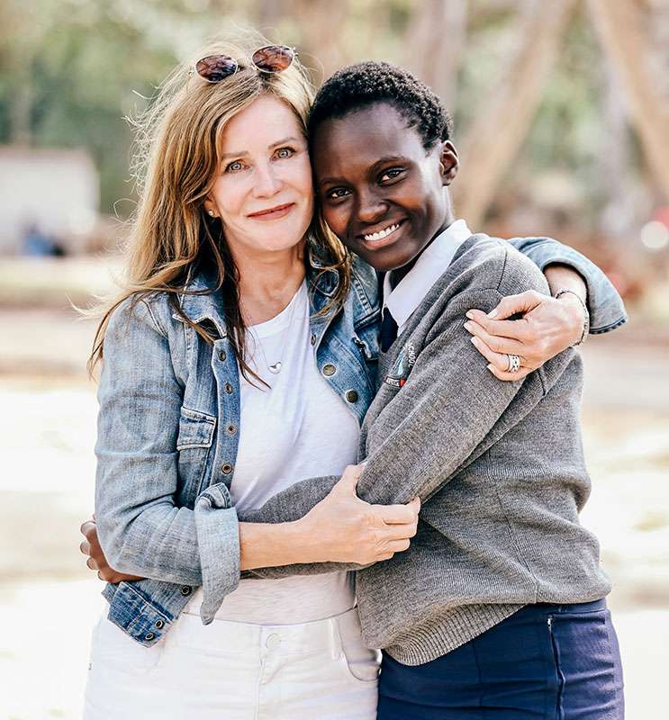 Lotte Davis wearing white dress and blue shirt hugging a smiling Kenyan girl future woman leader