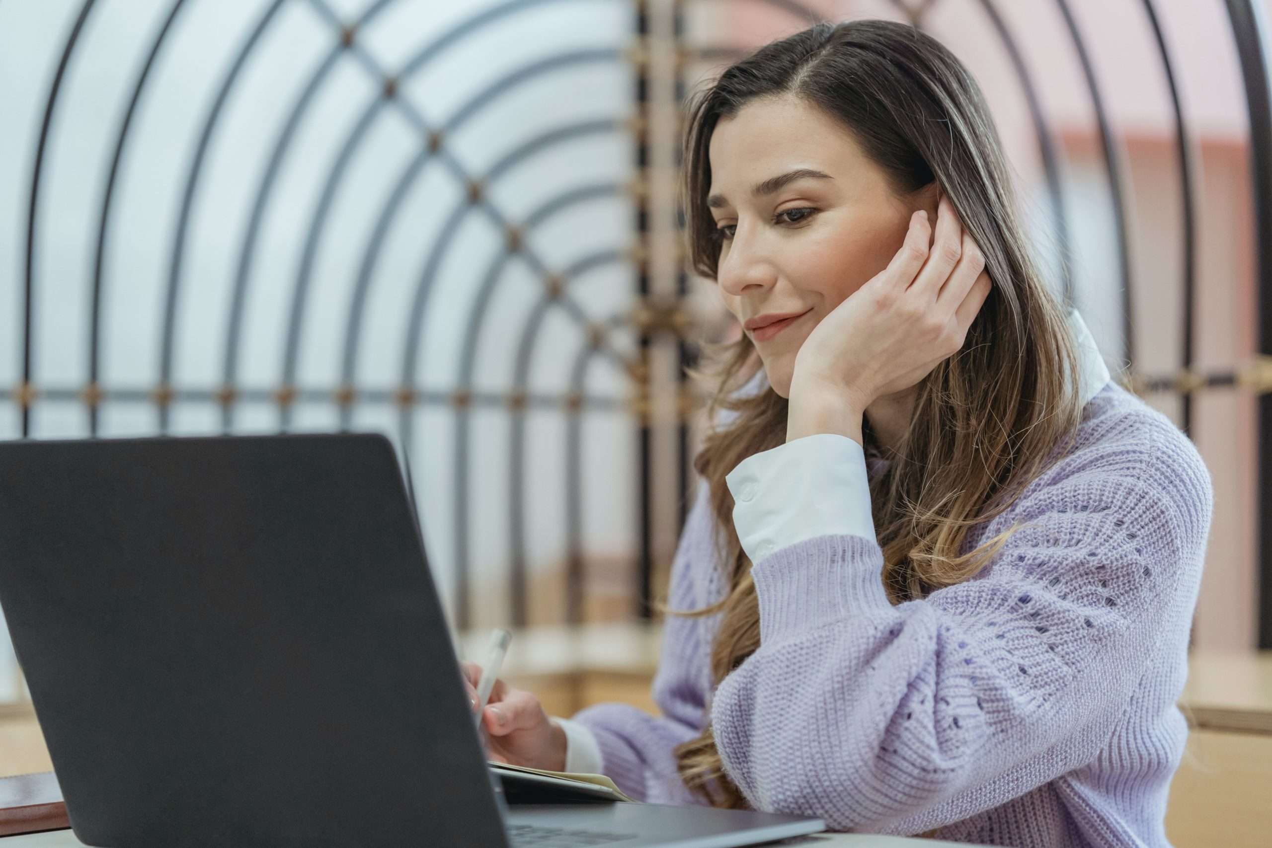 A woman smiling while looking at a laptop and writing.