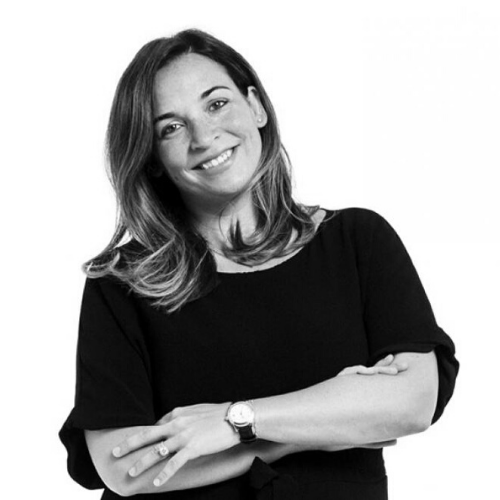 A woman with shoulder-length hair smiles, arms crossed, wearing a black top and watch, posing against a plain white background.
