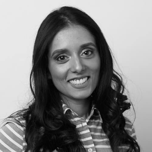 A woman with long, dark hair wearing a striped shirt smiles at the camera against a plain background.