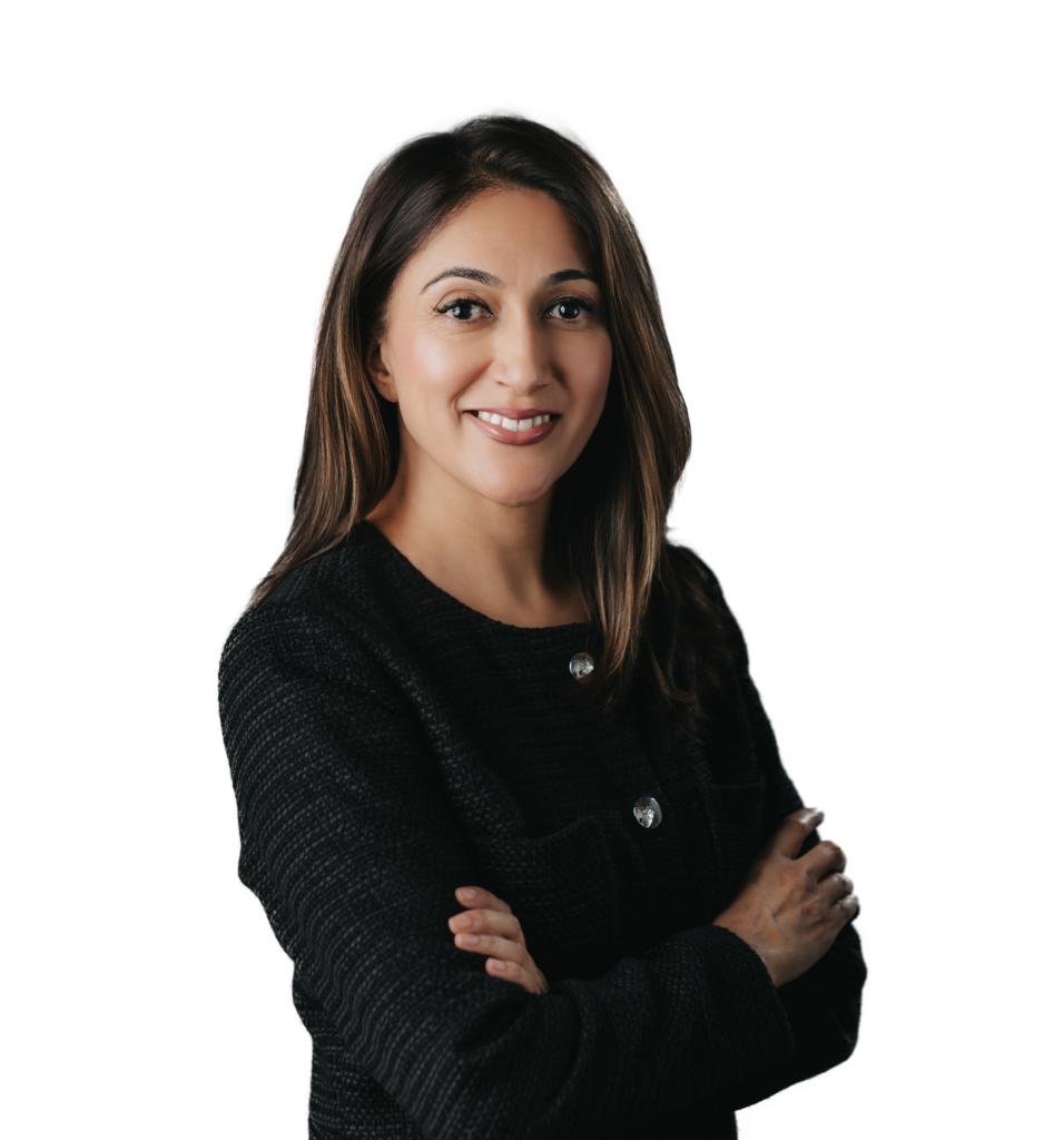 A woman with long brown hair wearing a black textured jacket stands against a plain white background, smiling with her arms crossed.
