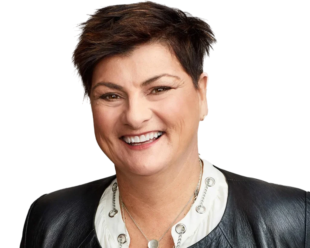 Smiling person with short dark hair, wearing a black leather jacket over a white top with silver details and a necklace, against a plain white background.