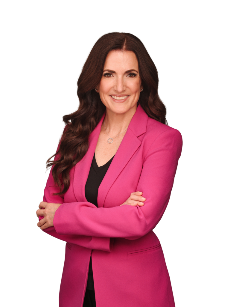 A woman with long brown hair, wearing a bright pink blazer and black top, stands smiling with arms crossed against a plain white background.